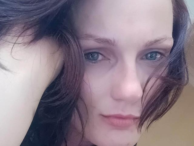 Sympathy has pale skin, blue eyes, and dark brown, slightly messy hair, with a small nose and pink lips, looking directly at the camera with a neutral expression.