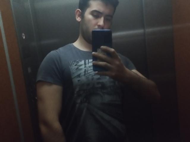 RodriinSanorp with a dark gray t-shirt, muscular arms, short black hair, and a beard, taking a mirror selfie in an elevator using a blue smartphone.