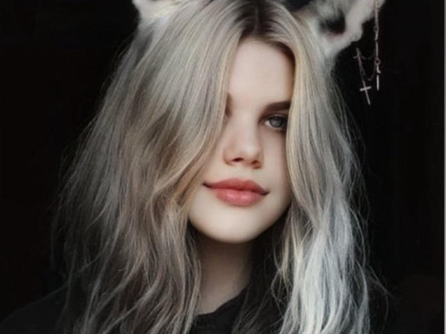 JoannLowe with long, silver-gray hair, cat ears, pale skin, and pink lips, smiling slightly. She has one eye covered by her hair, looking cute and sexy.