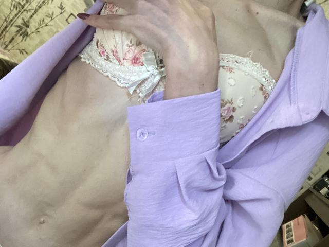 De roze, bloemenprint BH van Kabblasha, die kleine borsten laat zien, zit onder een lila shirt, waardoor een slank, vlak borstgedeelte zichtbaar is met zichtbare ribben en een platte buik..