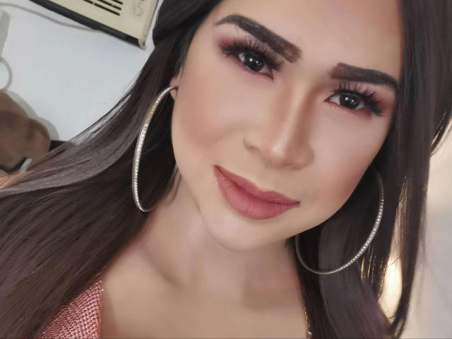 transsweetdenise-hot with long brown hair, wearing large hoop earrings, pink eyeshadow, and pink lipstick, smiling at the camera, showing off her cute face and pretty makeup.