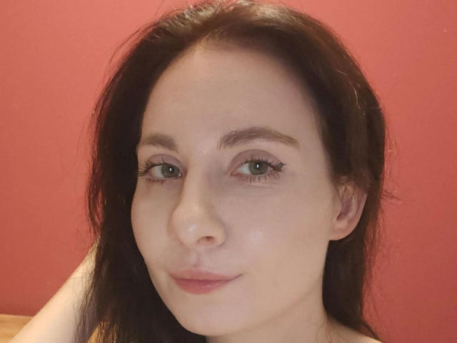 NettePaloma-hot has pale skin, green eyes, and dark brown hair. She's smiling with a slight pink lip color, looking at the camera. Her tits are not visible.