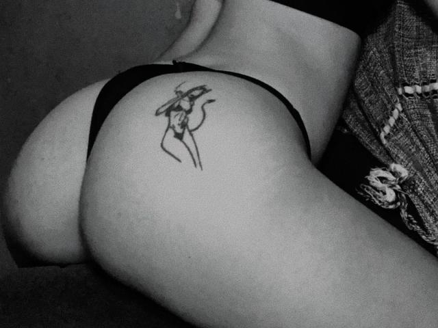 CasalMisterioso's ass is in black thong underwear, showing a tattoo of a stick-figure woman with arms raised. Greyscale photo, focus on butt and tattoo.