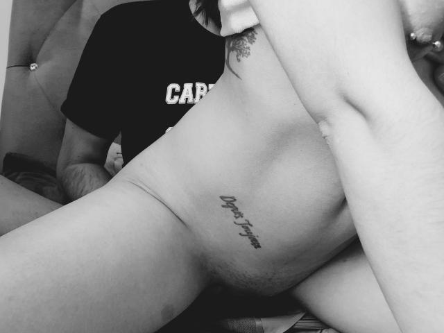 Black-and-white photo of EncuentroIntimo's nude lower body, showing a tattoo on the right side of the pelvis, with a partially visible man in a dark shirt.