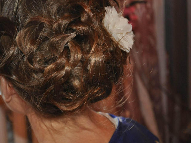Keiri's curly brown hair in an elegant updo, featuring a white floral hairpiece, with subtle highlights and a slightly wavy texture, showing off her delicate, stylish look.
