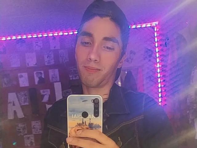 LucasSmith with a slight smirk, wearing a black denim shirt, holding a phone with a city skyline case, purple LED strip lights in the background.