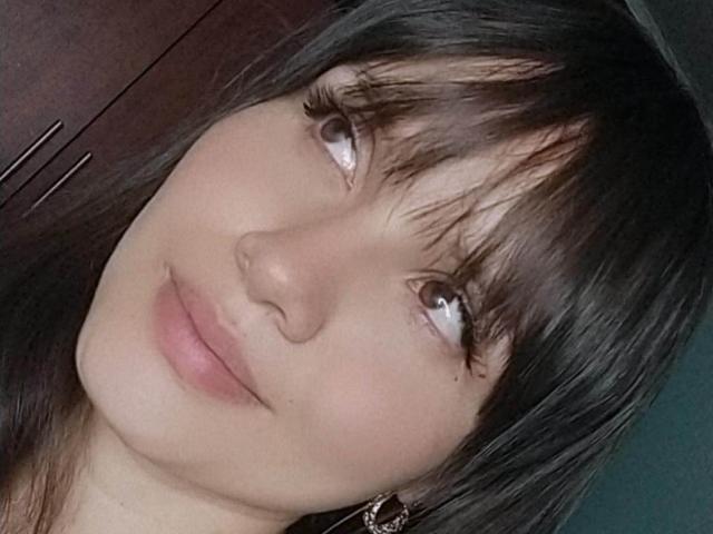 AliceMoon69's face with black hair, bangs, and long eyelashes, looking slightly up with a soft smile, showing light pink lips and fair skin.