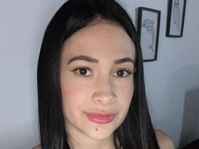 CherryLoux with straight black hair, brown eyes, and pink lips, wearing no clothes, showing a small beauty mark below her right lip. Her tits are not visible.
