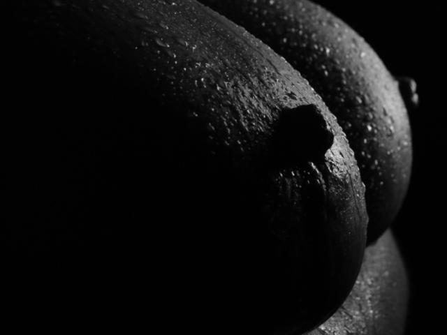 Black and white photo of RoxolanaSexy's wet, textured, dark-skinned boobs with droplets of water and a prominent nipple in shadowy, close-up detail.