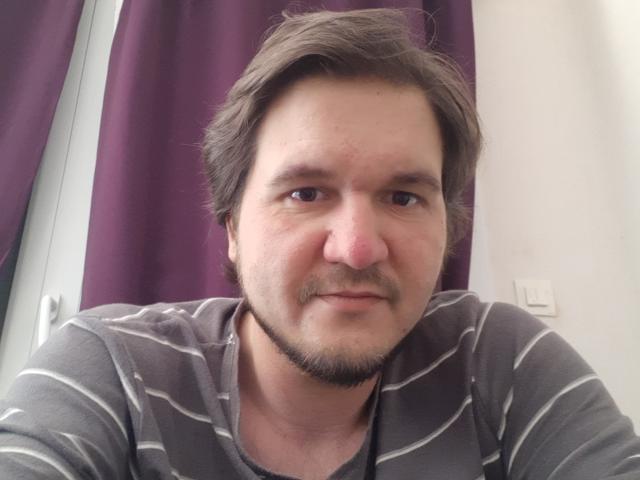 NectarineFad has a chubby face, brown wavy hair, small goatee, and is wearing a grey and white striped shirt. His nose is slightly red.