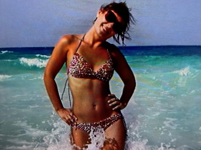 DianaAhTender in a leopard print bikini, standing in the ocean with water splashing, wearing sunglasses, hands on hips, smiling, and showing her tan, toned, and curvy ass.