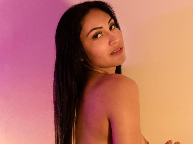 LanaBox has long black hair, looking over her shoulder with a slight smile. She's topless, showing her bare back and a small mole on her cheek.