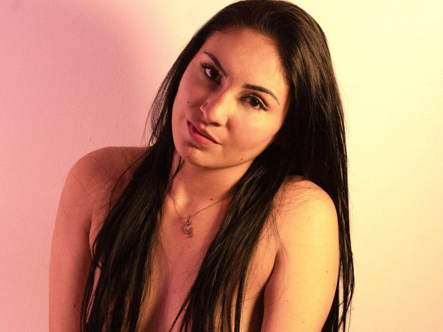 LanaBox has long black hair, light skin, and a small nose piercing. She's topless with visible breasts and a necklace, looking slightly to the side with a subtle smile.