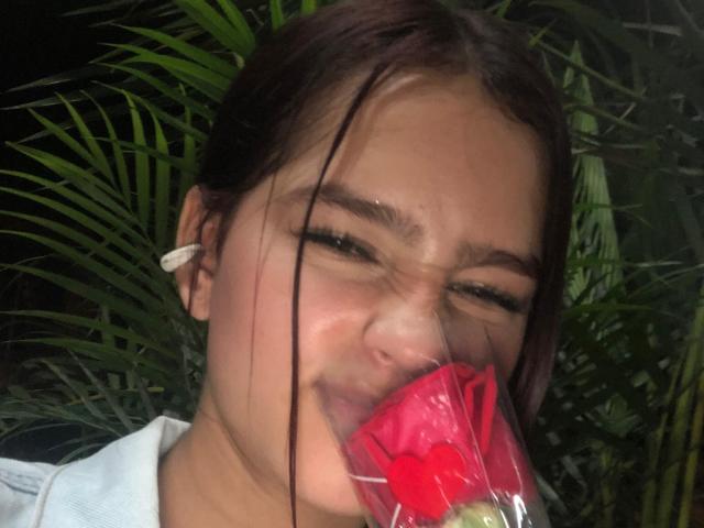 MelodyMansson's face is squished with eyes shut, holding a red plastic cup with a straw in her mouth, brown hair in a messy bun, white ear clip on.