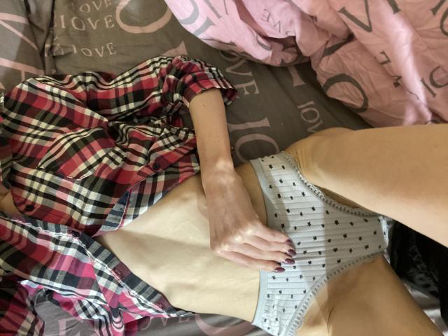 Kabblasha è sdraiata su un letto, indossa una camicia a quadri rossa, biancheria intima bianca con pois neri, e ha una mano appoggiata sulla sua pancia piatta, chiara, esile e nuda..