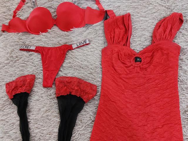 Conjunto de lingerie vermelha, incluindo um sutiã vermelho, uma tanga de renda vermelha, uma blusa de renda vermelha e meias vermelhas com detalhes em renda preta. Os seios da NewCrystal são exibidos no sutiã e na blusa..