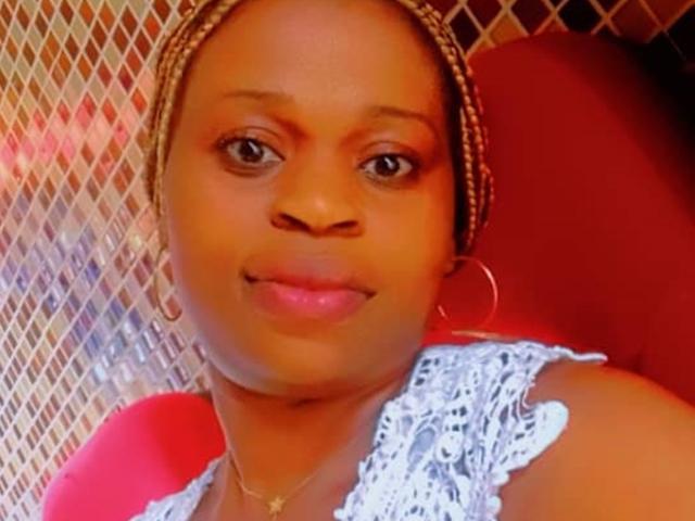 TierraX with dark brown skin, braided hair, hoop earrings, wearing a lace top, smiling, pink lips, small gold necklace, red background, and chain-link pattern on the left.