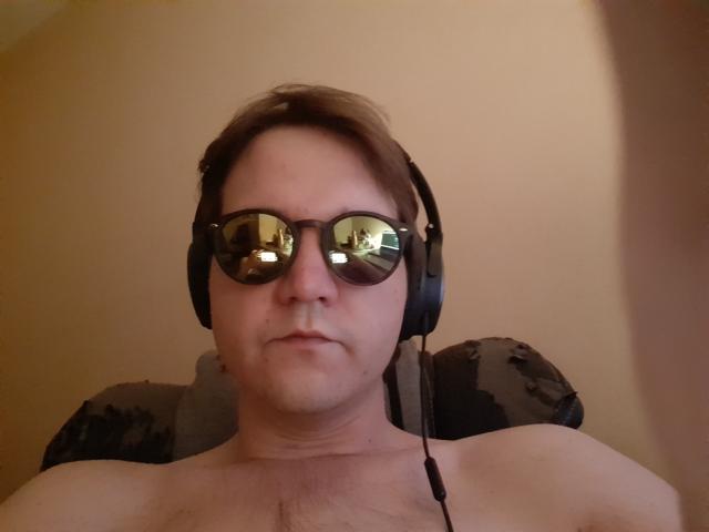 NectarineFad is a shirtless dude with reflective sunglasses and black headphones, looking slightly annoyed. His chest is hairy, and the photo is taken from a low angle.