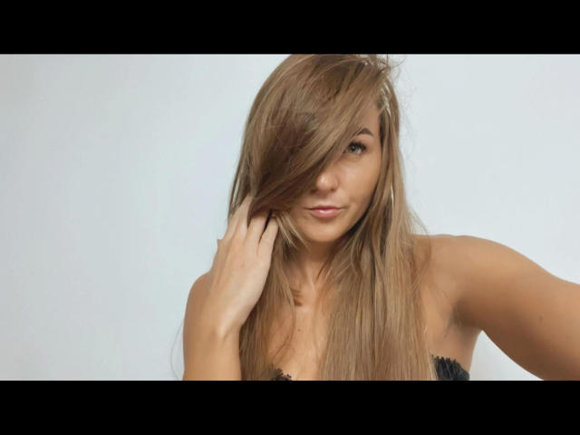 GanzNettePaola-hot with long brown hair, covering one eye, slight smile, hand in hair, black strap top, light skin, sexy, subtle makeup, soft light, simple background.