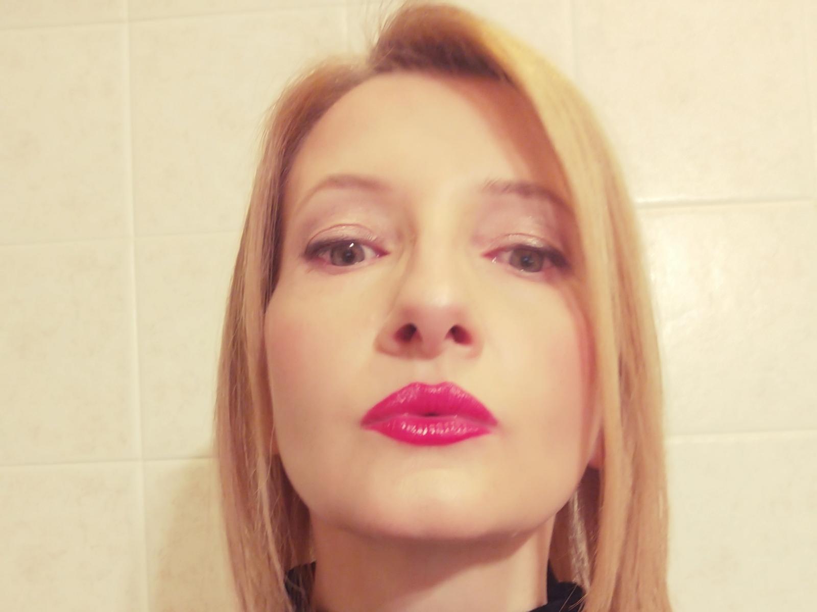OrchideaHots has blonde hair, pink lipstick, and light makeup with slightly blurry eyes, looking up at the camera. Her ass is not visible.
