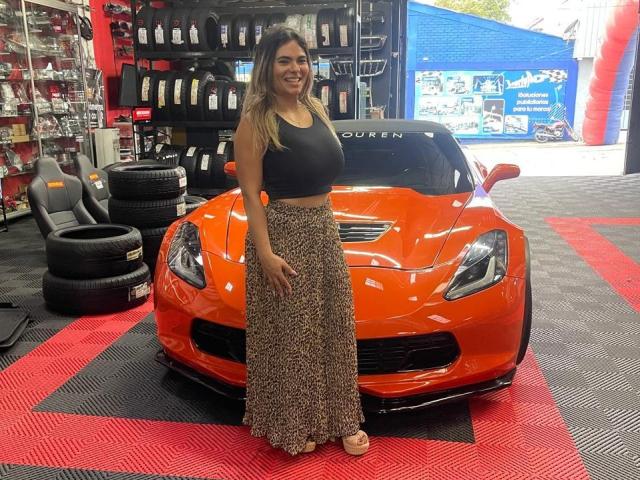BrianaPreston stands in front of a shiny red sports car, wearing a black crop top and a long leopard print skirt, showing her large ass and tits.