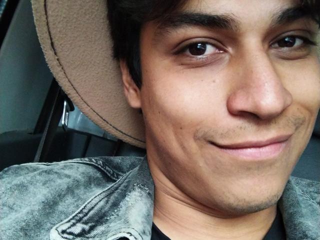 Lestatd's face with a slight smile, brown eyes, and short dark hair, wearing a beige hat and grey, worn-out jacket. Lestatd's nose is small and his skin is tan.