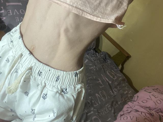 Kabblasha's slim, pale, ribbed belly with visible ribs wearing white, patterned pajama pants, and a pink shirt. The waistband is slightly raised.
