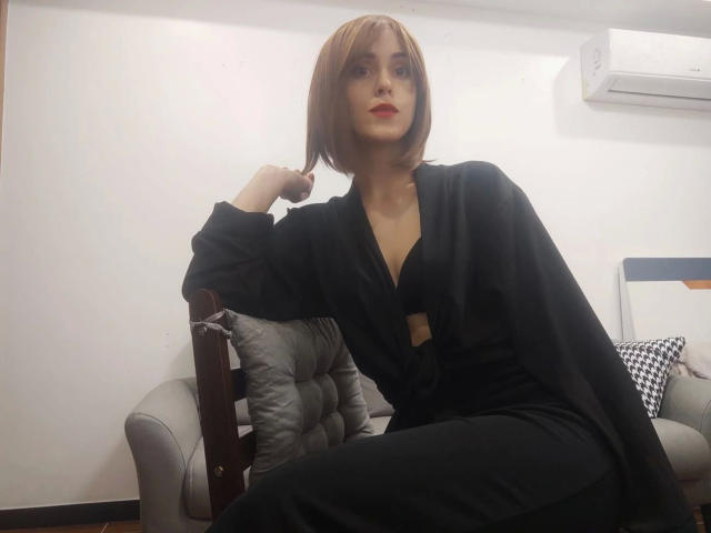 KnackigeOssi-hot with short brown hair, black dress, and red lipstick, sitting on gray chair, hand on head, looking at camera, air conditioner above, black pants, confident pose.