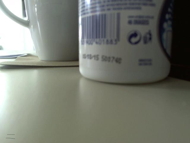 White ceramic mug with barcode and blue text, next to a similar white mug, on a light-colored surface. Boobs are not visible. Olegator-hot is not in the image.