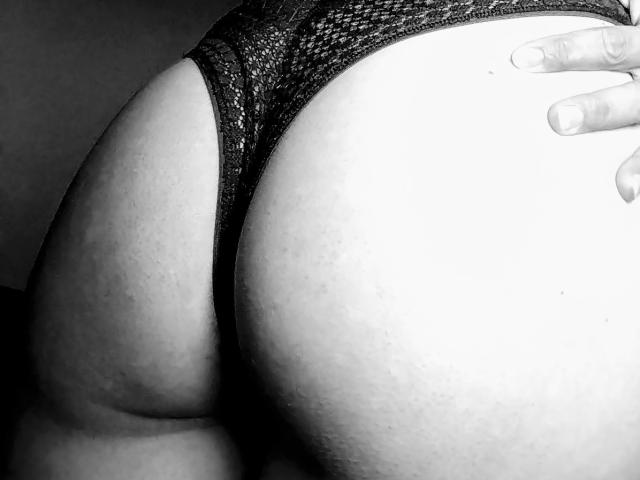 SensuelleMoon's ass in black lace panties, showing her large, round butt with a hand resting on her right cheek. Black and white photo, emphasizing her curvy, sexy shape.