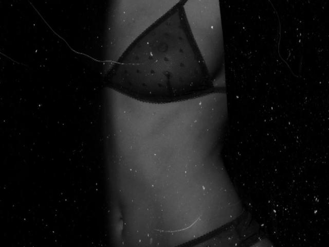 MarinaTender's slim, toned torso with small, dark mesh panties and a matching bralette. The black and white image highlights her flat stomach and subtle curves.