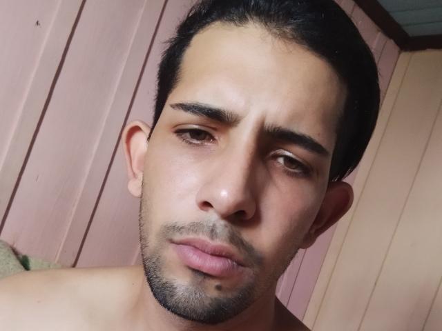 Il viso di Donino, con i capelli scuri e leggermente disordinati, gli occhi marroni, un leggero pelo e una piccola lentiggine sotto il labbro destro. Ha un'espressione seria, con un leggero sbuffo. Senza camicia..