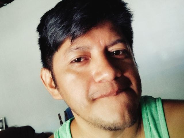 AxelLatino has short black hair, brown eyes, and a slight smile with a green tank top, showing a cute, chubby face with a light stubble.