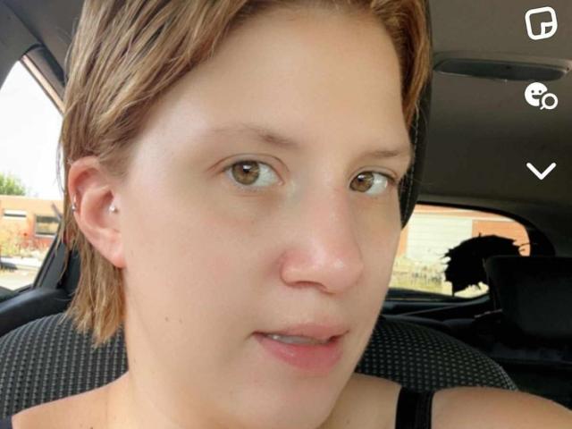 MireilleM has light brown eyes, short brown hair, and is wearing a black top. Her face is slightly turned, showing a small ear piercing. She's sitting in a car.