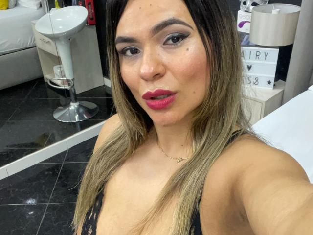 BrianaPreston with medium tits, wearing a black lace top, pink lipstick, and a gold necklace, has straight, blonde-highlighted hair, and is pouting in a selfie.