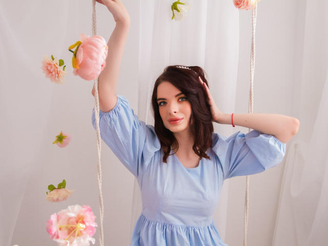 AdeleClifford with pale skin, dark brown wavy hair, blue eyes, wearing a light blue dress, holding pink flower lanterns, arms raised, white curtain backdrop, red bracelet.