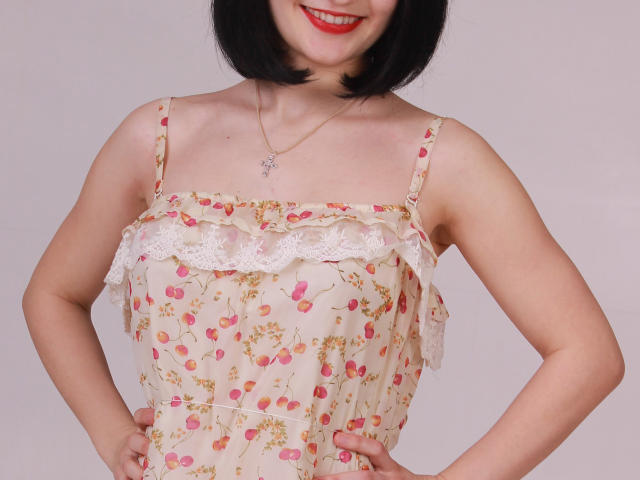 GloriaUpperLove has a cute smile, wearing a floral dress with lace trim, showing her small tits and arms, black bob haircut, and a delicate necklace.