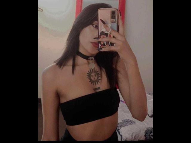SalomeMille heeft donker haar, een zwarte choker met een zonnetattoo, en een zwarte top zonder bandjes, die haar borsten en een getatoeëerde borst laat zien op een spiegelzelfportret..