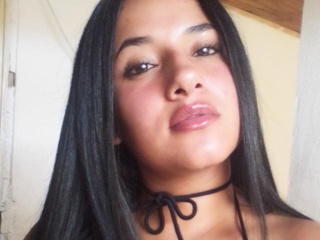 Ansol has shiny black hair, brown eyes, pink glossy lips, and a black choker with a knot. Her skin is a warm brown tone, and she's looking slightly up.