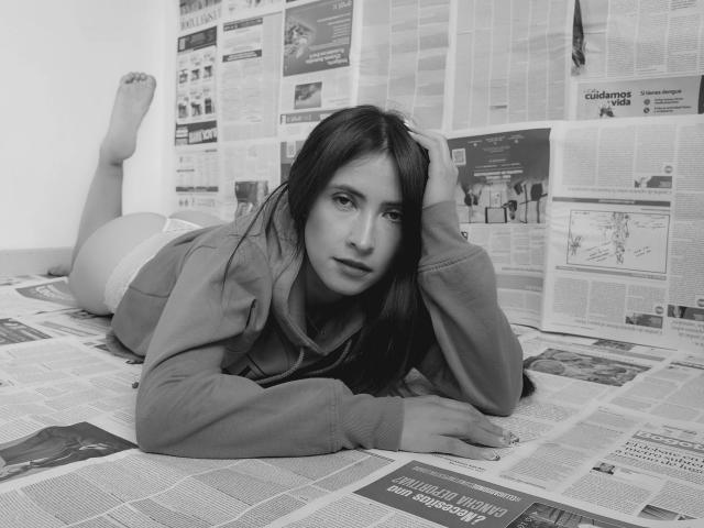 JainaRogers, lying on newspaper, wearing a hoodie, white panties, barefoot, dark hair, looking at camera, hand in hair, ass up, relaxed, black-and-white, realistic, soft expression.