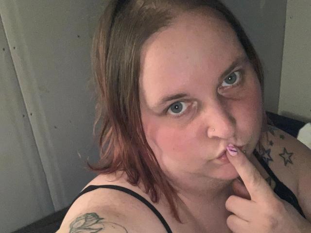 Kiramaus88-hot with pink lipstick, brown hair, blue eyes, nose piercing, finger in mouth, black tank top, star tattoos, pink nail polish, slightly flushed face, and a relaxed expression.