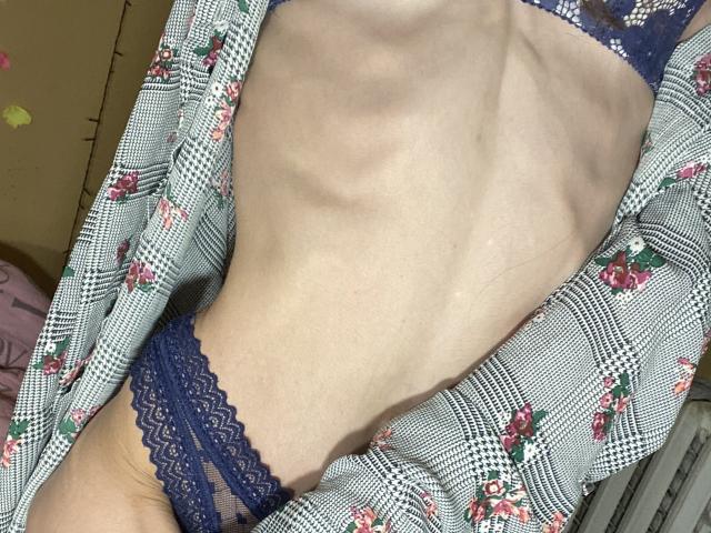 El torso delgado, pálido y plano de Kabblasha, con costillas visibles, vestía unos panties de encaje azules y una bata con estampado floral, ligeramente abierta. El pequeño y plano trasero de Kabblasha es parcialmente visible..
