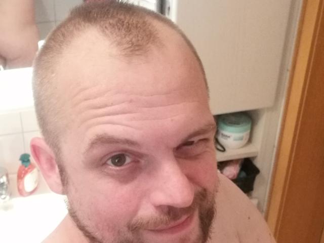 DonGranato69 with a balding head, winking, light brown beard, and slight smile, looking at the camera. His face is slightly wrinkled, and he's shirtless.