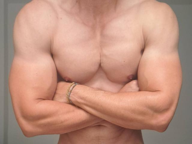 AtleticoMaduro's muscular, shirtless chest with crossed arms, showing defined pectorals and biceps, wearing a gold bracelet on the right wrist. Fair skin, slightly visible nipples.