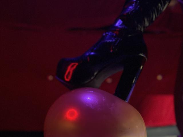 PerlaDivaio's shiny black stiletto heel with a red "8" on the side, resting on a purple and red lit, glossy, spherical object.