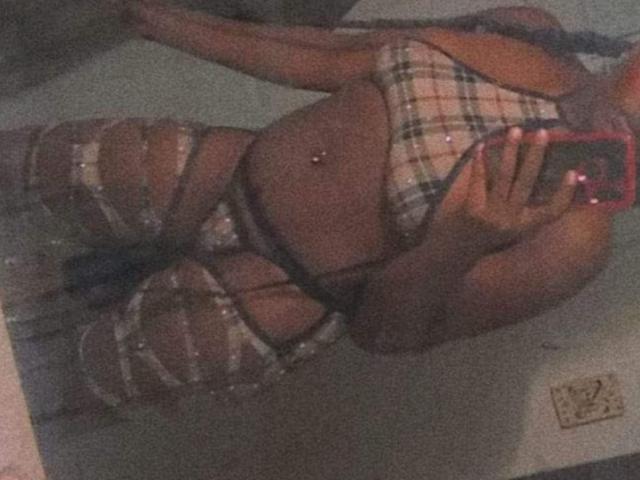 SheaButta wearing a plaid bikini top and torn, glittery, strappy bottoms showing her large tits and round ass. She's holding a pink phone, with a navel piercing.