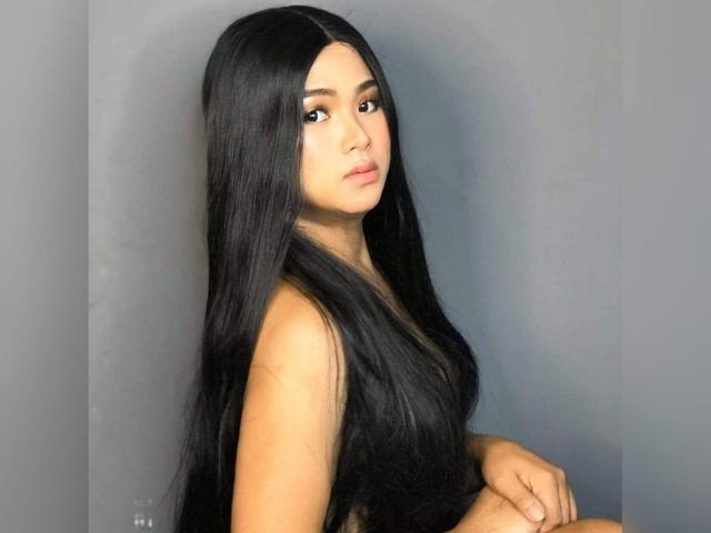 TreatMeLikeAQueen with long, straight black hair, looking over shoulder, has light brown skin and is wearing a sleeveless top, showing her small, perky ass.