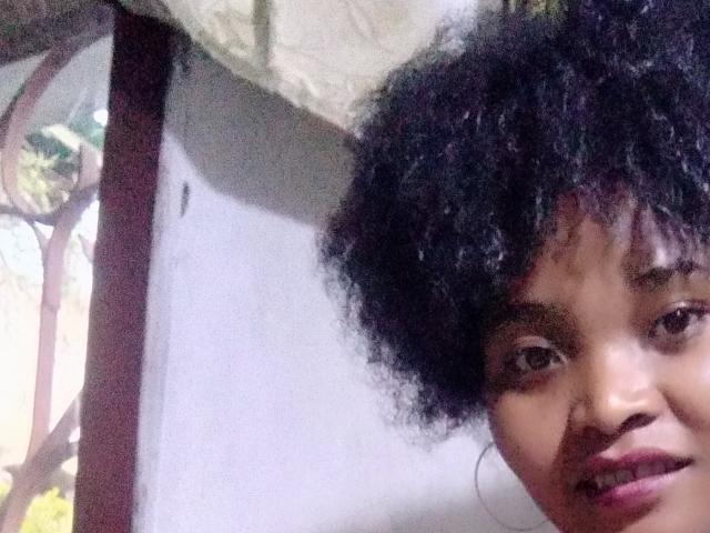 Gelisca's face with curly black hair, brown eyes, and a slight smile, showing her nose and upper lips. Her hoop earrings are barely visible. She's looking at the camera.