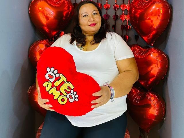 AliceShae has a fat ass, holding a red heart pillow with "pawo" on it. She's wearing a white shirt, dark pants, and red lipstick, with shiny red heart balloons.