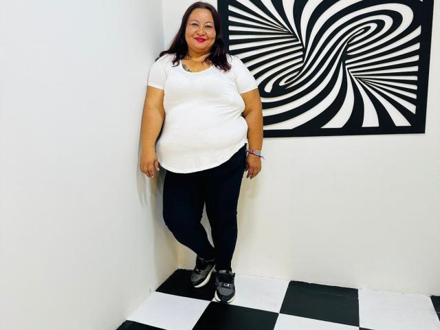 AliceShae with medium tits, a chubby ass, dark brown hair, red lipstick, white shirt, black pants, and black sneakers, standing on a black-and-white checkered floor.